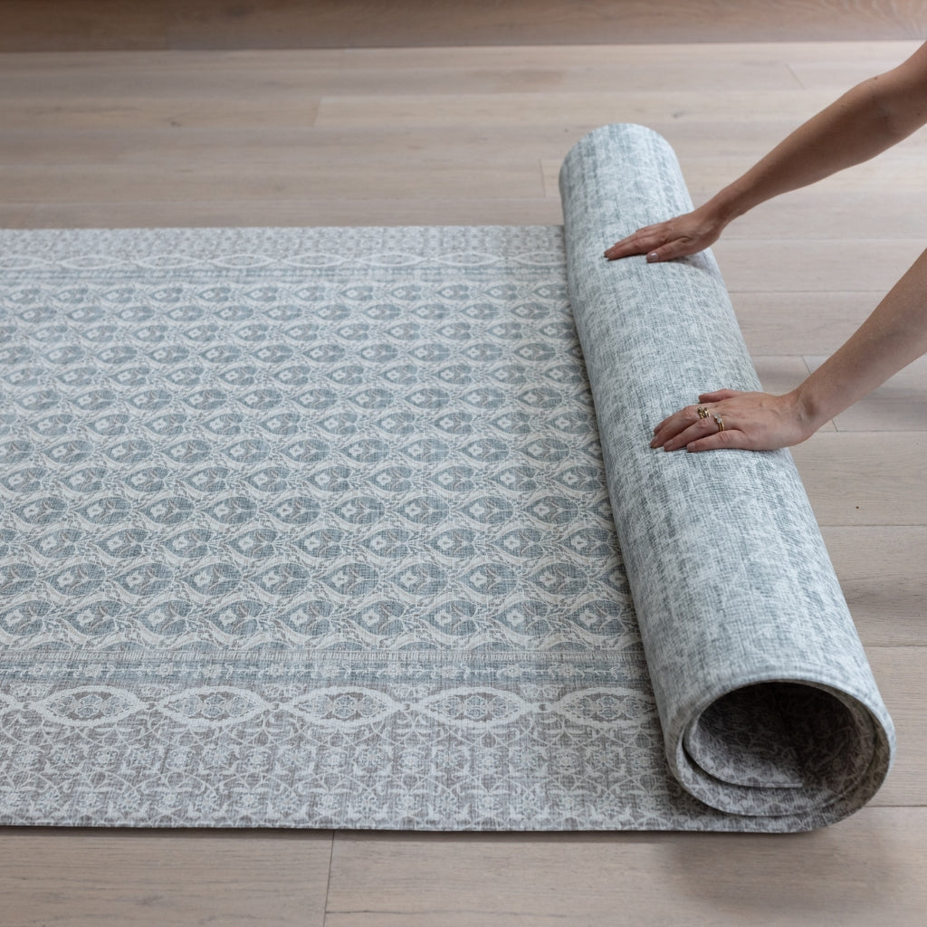 Hands roll up a large baby play mat with a hazy blue-gray medallion pattern  
