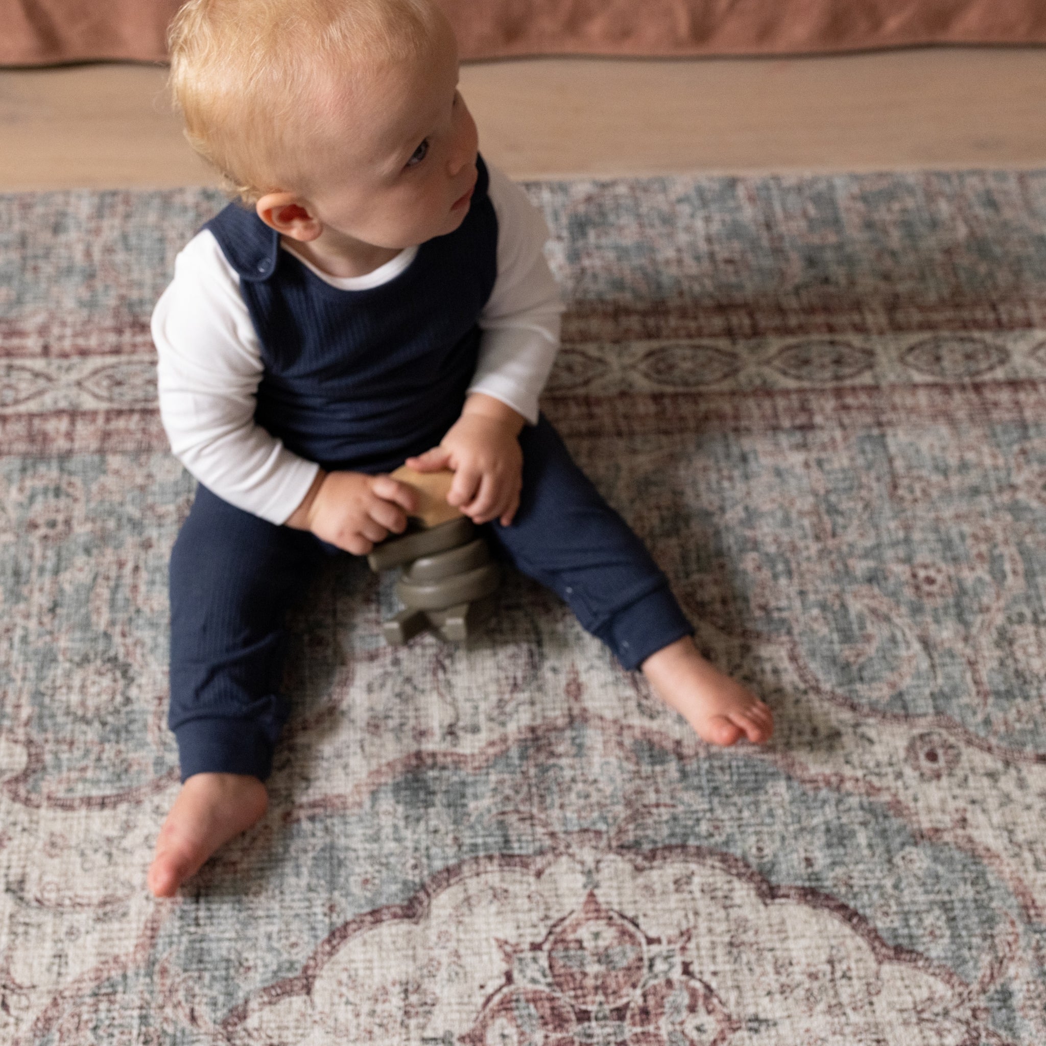 A baby sits on a soft floor mat that looks like a persian rug