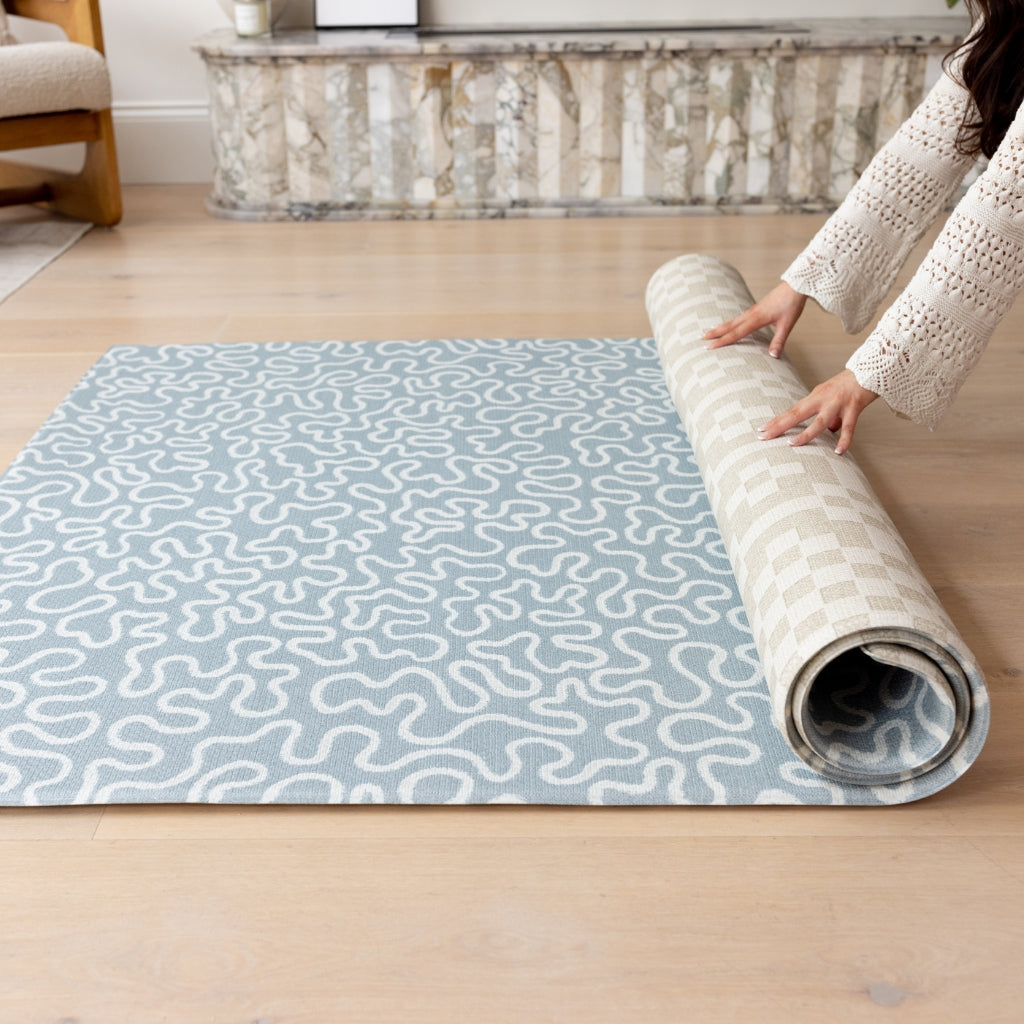 model unrolls a large play mat for toddlers in sea foam and neutral colors 