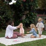 Woman and children playing outdoors on a wipeable memory foam play mat with trees and greenery in the background