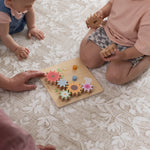 Two children playing with a wooden toy on  a patterned safe floral design play mat