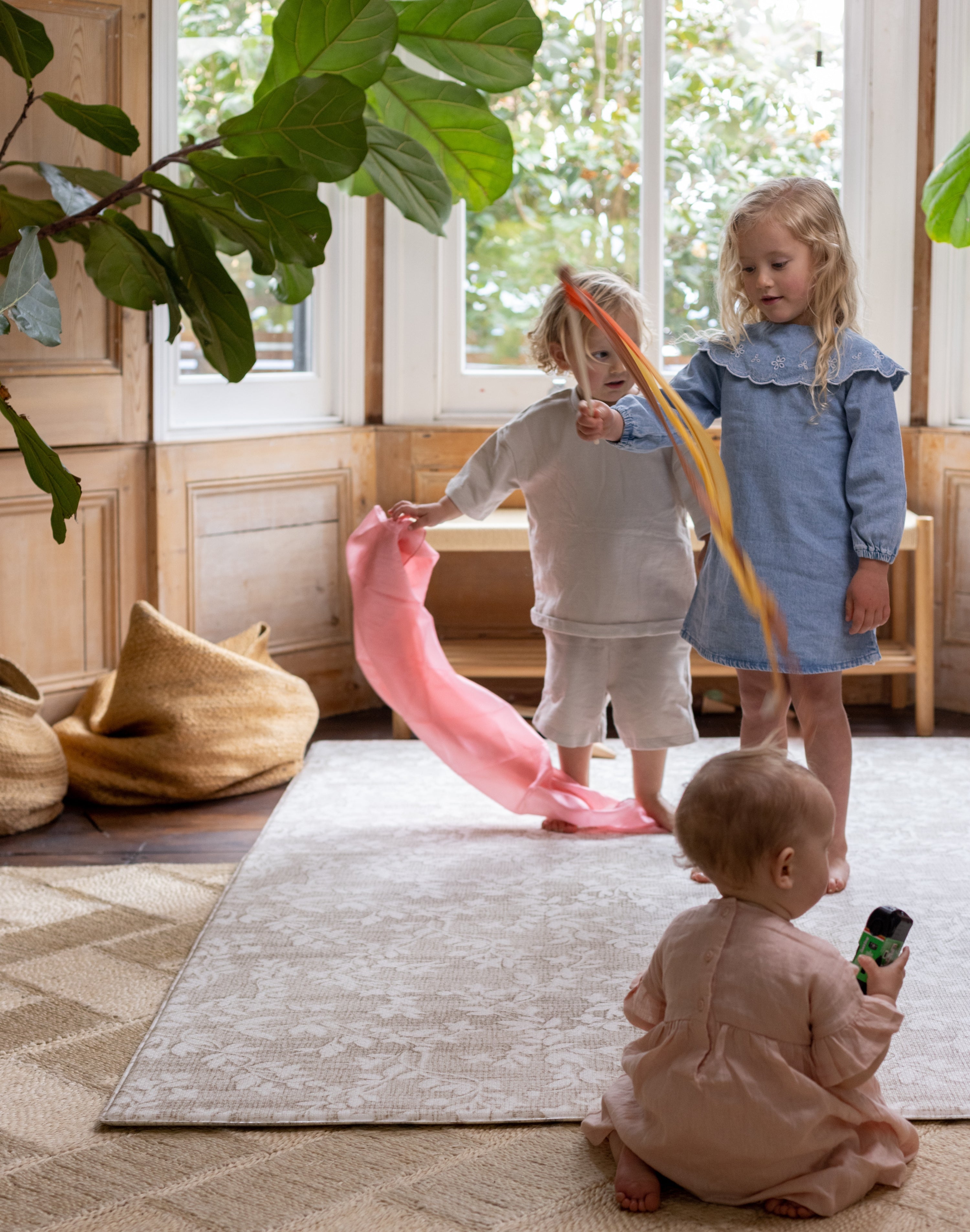 Three children playing on a floral rug-like play mat