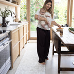 Woman holding a baby in a kitchen stood on a comfortable play mat rug-like runner