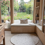 Cozy reading nook with a window seat, cushions, and a round floral rug-like play mat