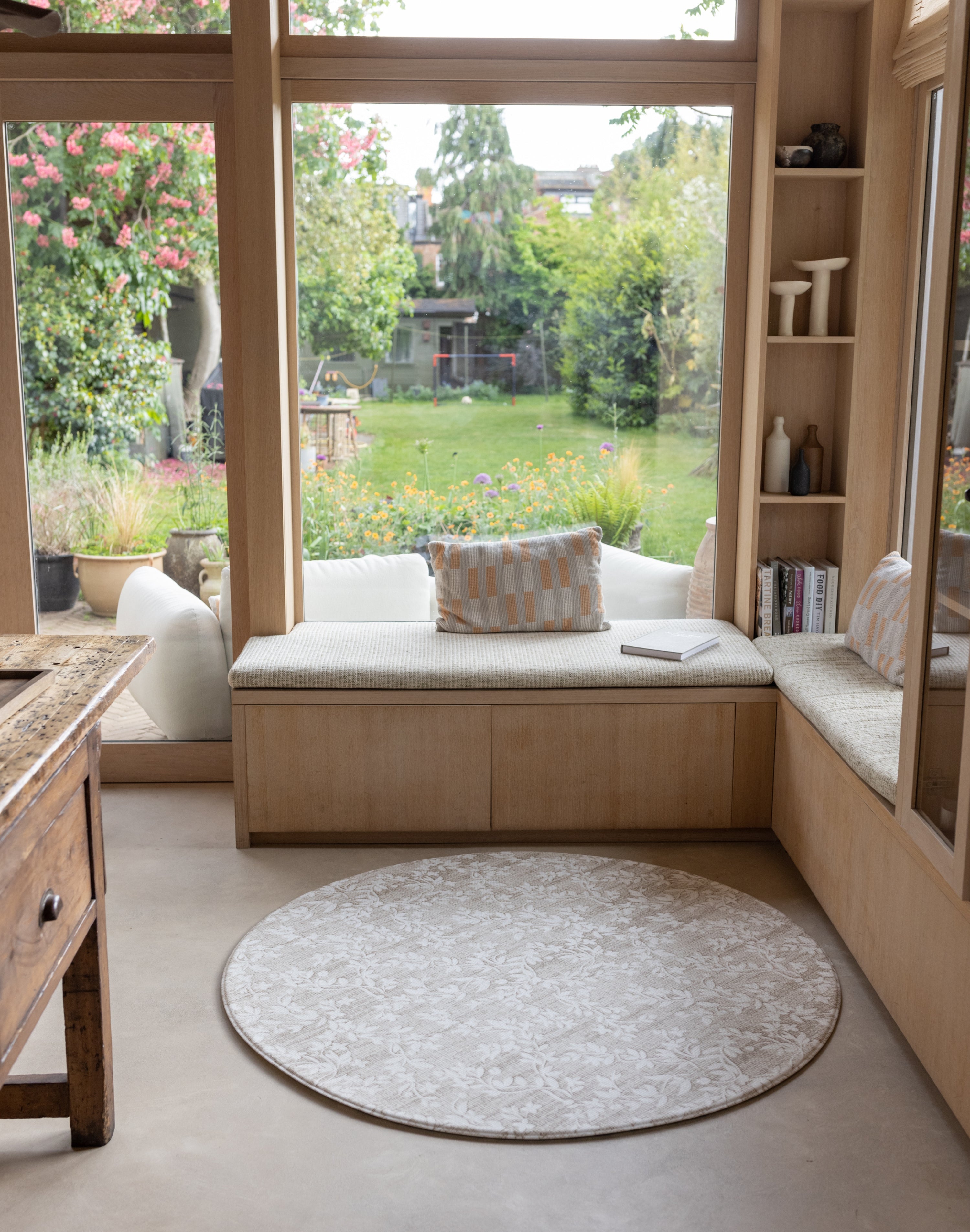 Cozy reading nook with a window seat, cushions, and a round floral rug-like play mat
