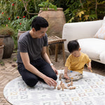 Man and child playing with wooden toys on a round, patterned comfortable play mat