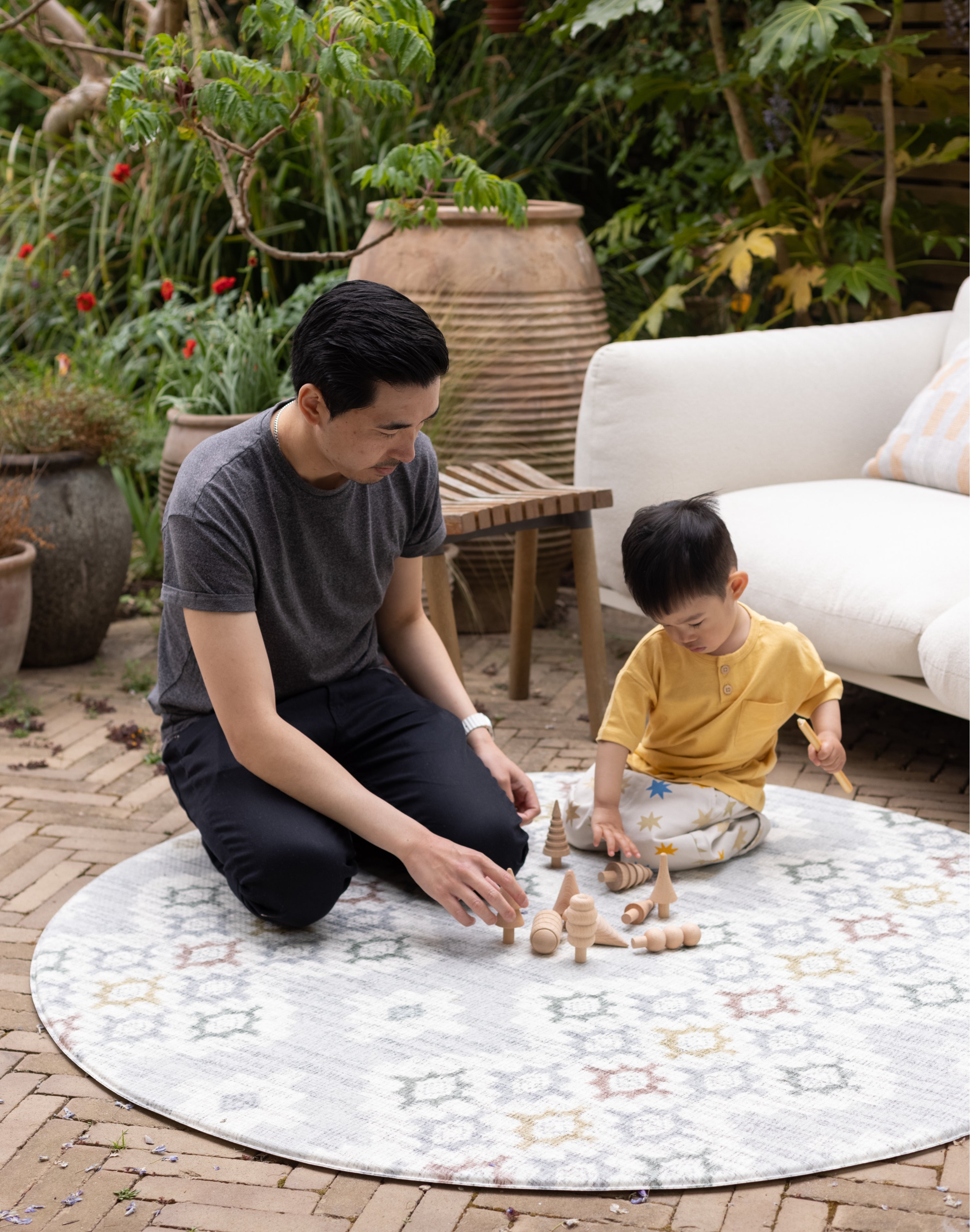 Man and child playing with wooden toys on a round, patterned comfortable play mat