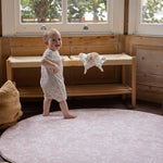 Baby standing on a round pink rug-like totter and tumble play mat 