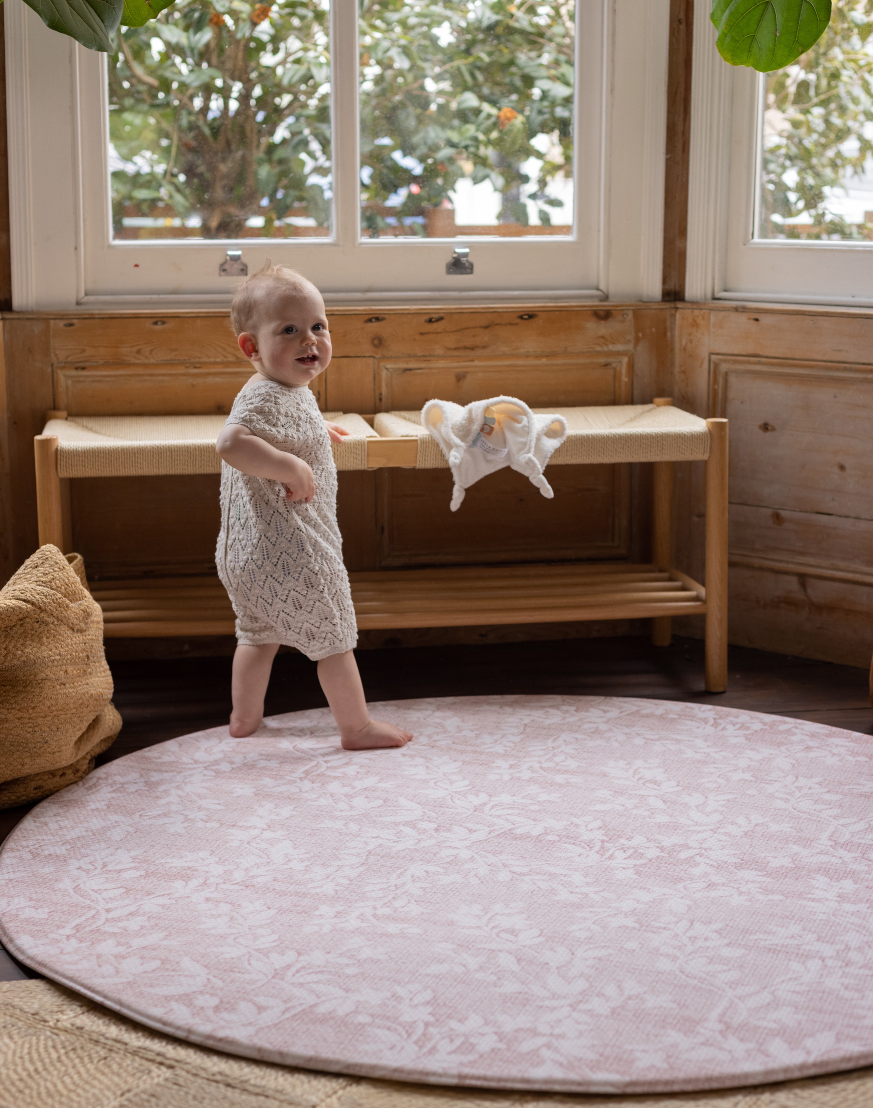 Baby standing on a round pink rug-like totter and tumble play mat 