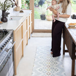Woman holding a baby in a kitchen stood on a comfortable memory foam baby safe play mat