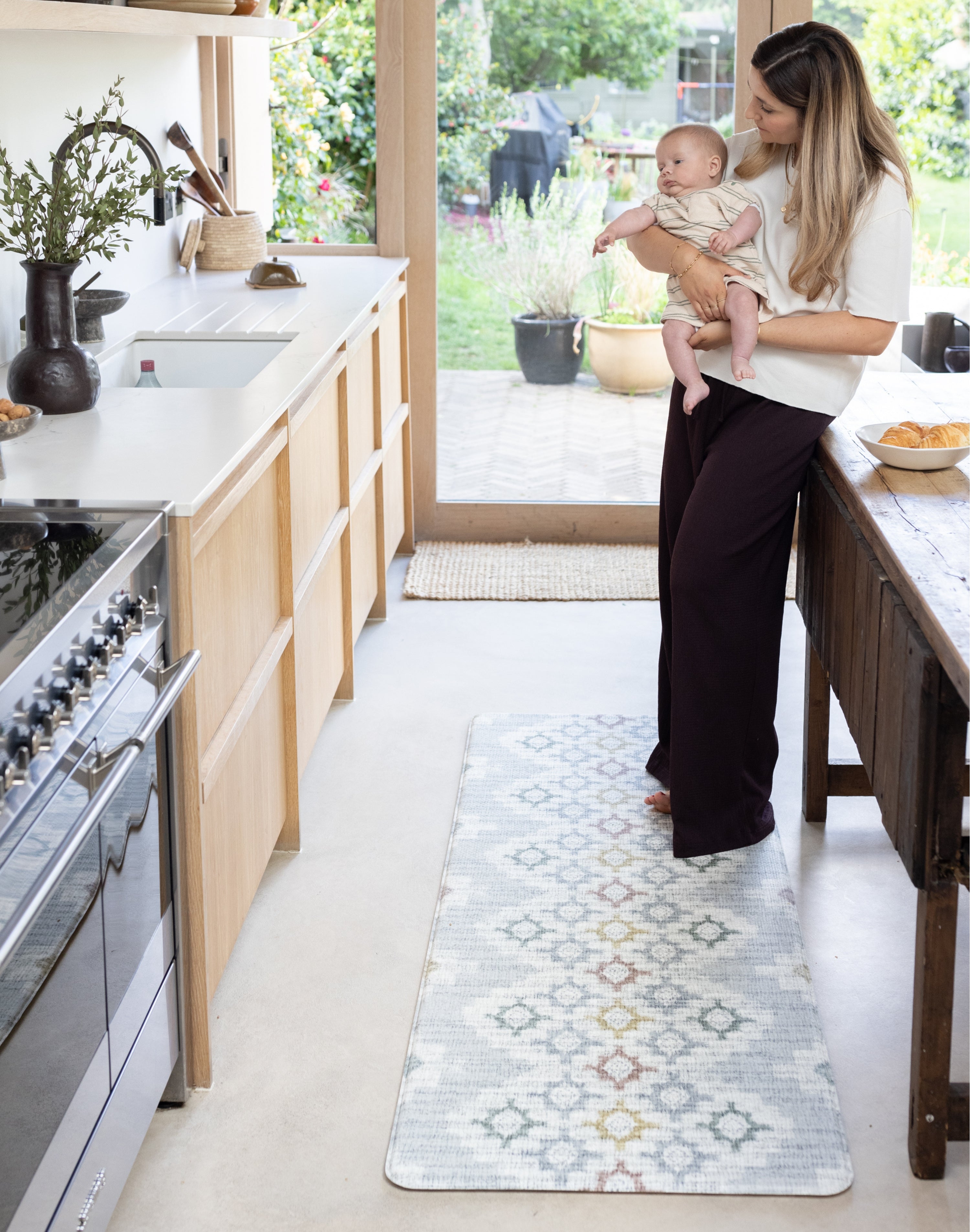 Woman holding a baby in a kitchen stood on a comfortable memory foam baby safe play mat