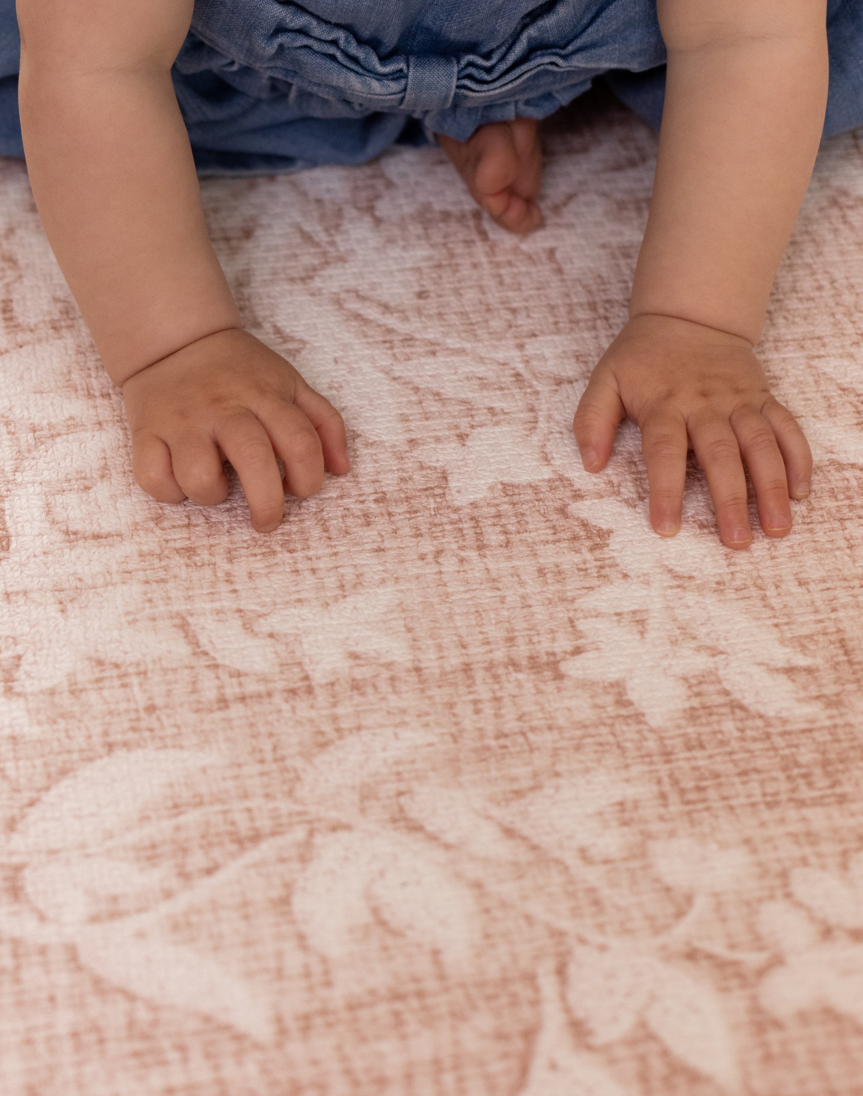 Close-up of a baby's hands on a patterned totter and tumble memory foam play mat