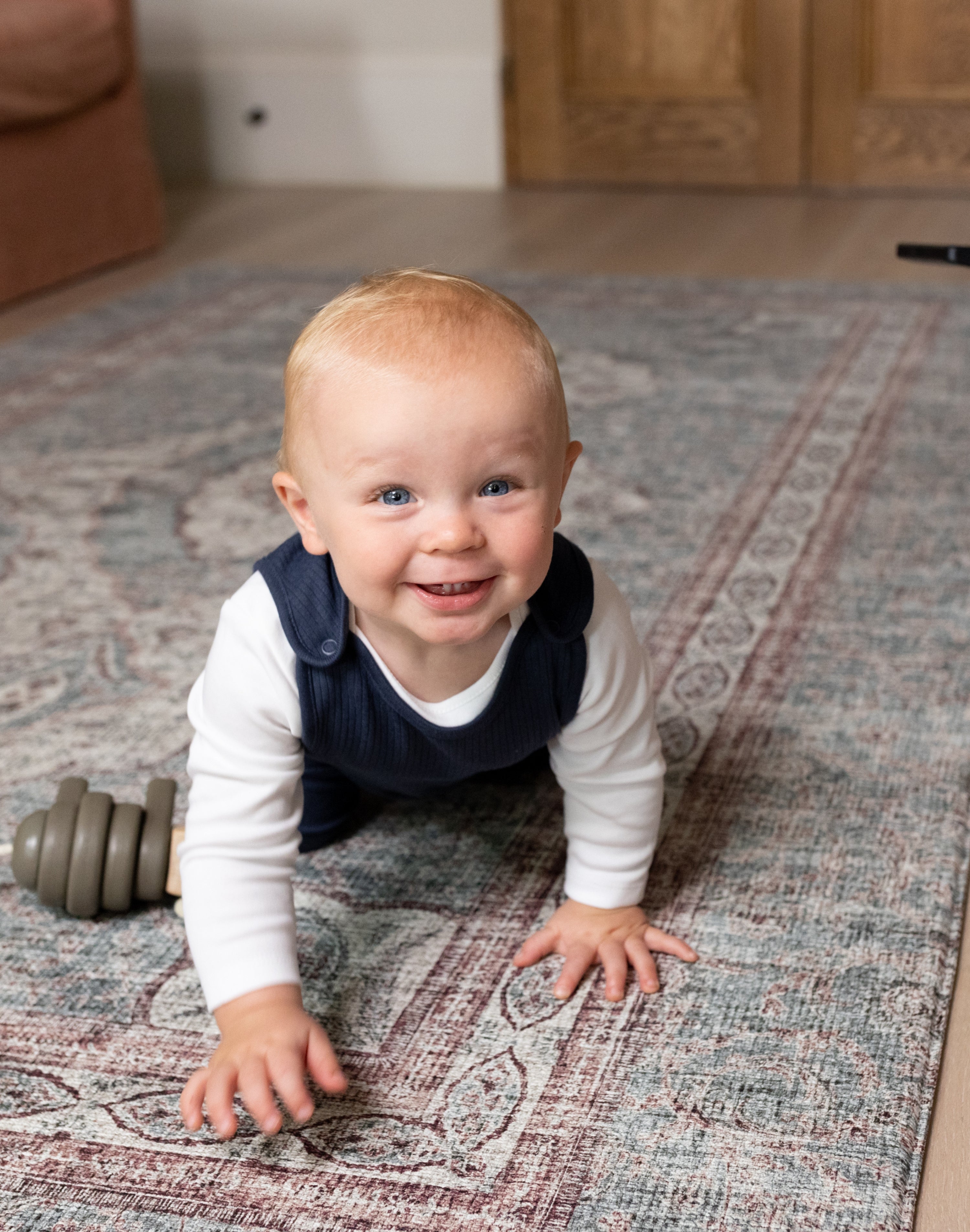Smiling toddler crawling on Totter + Tumble play mat enjoying safe playtime.