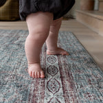 Toddler standing barefoot on soft Totter + Tumble patterned play mat.