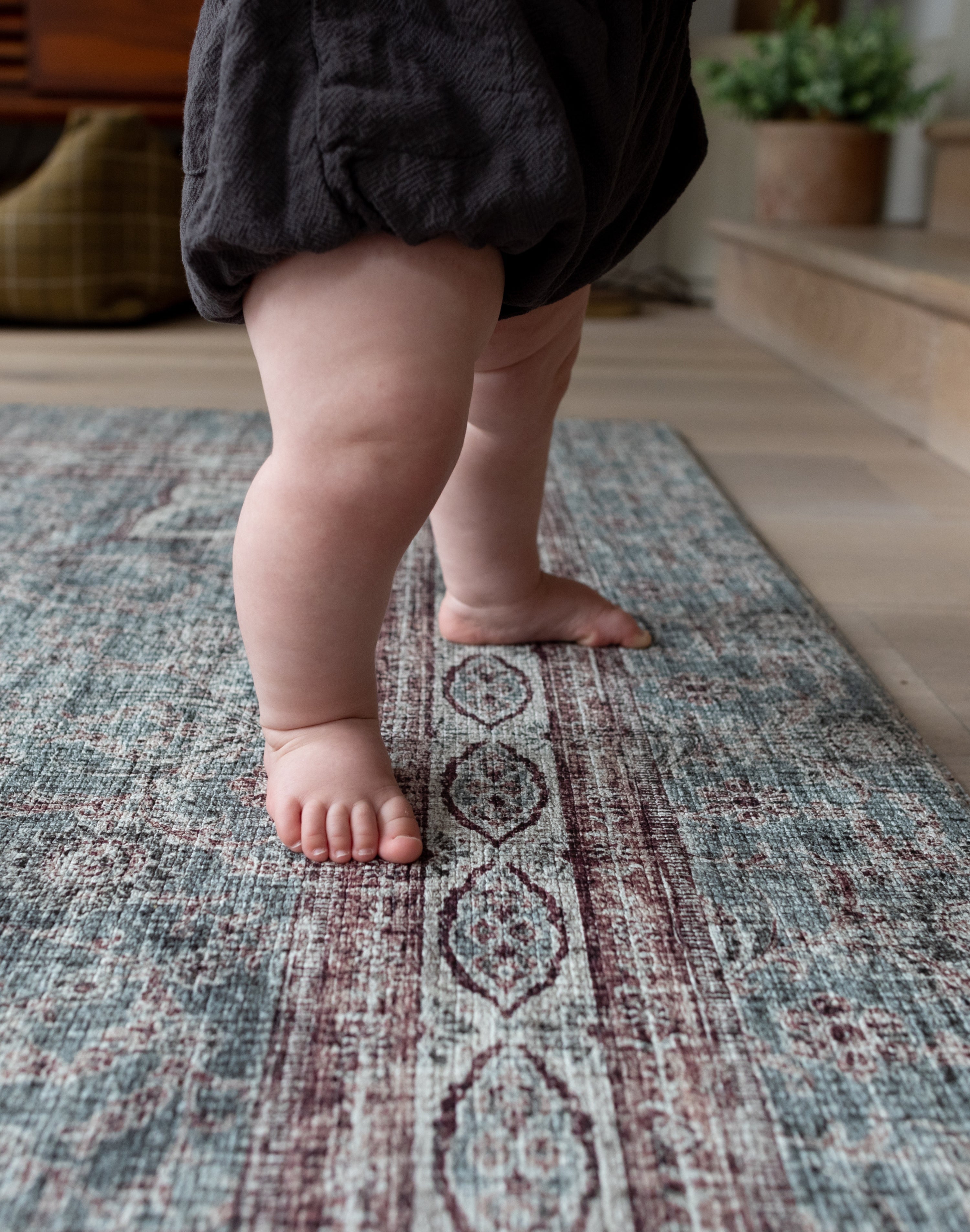 Toddler standing barefoot on soft Totter + Tumble patterned play mat.