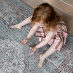 Toddler sitting on Totter + Tumble rug like playmat in a stylish lounge setting.