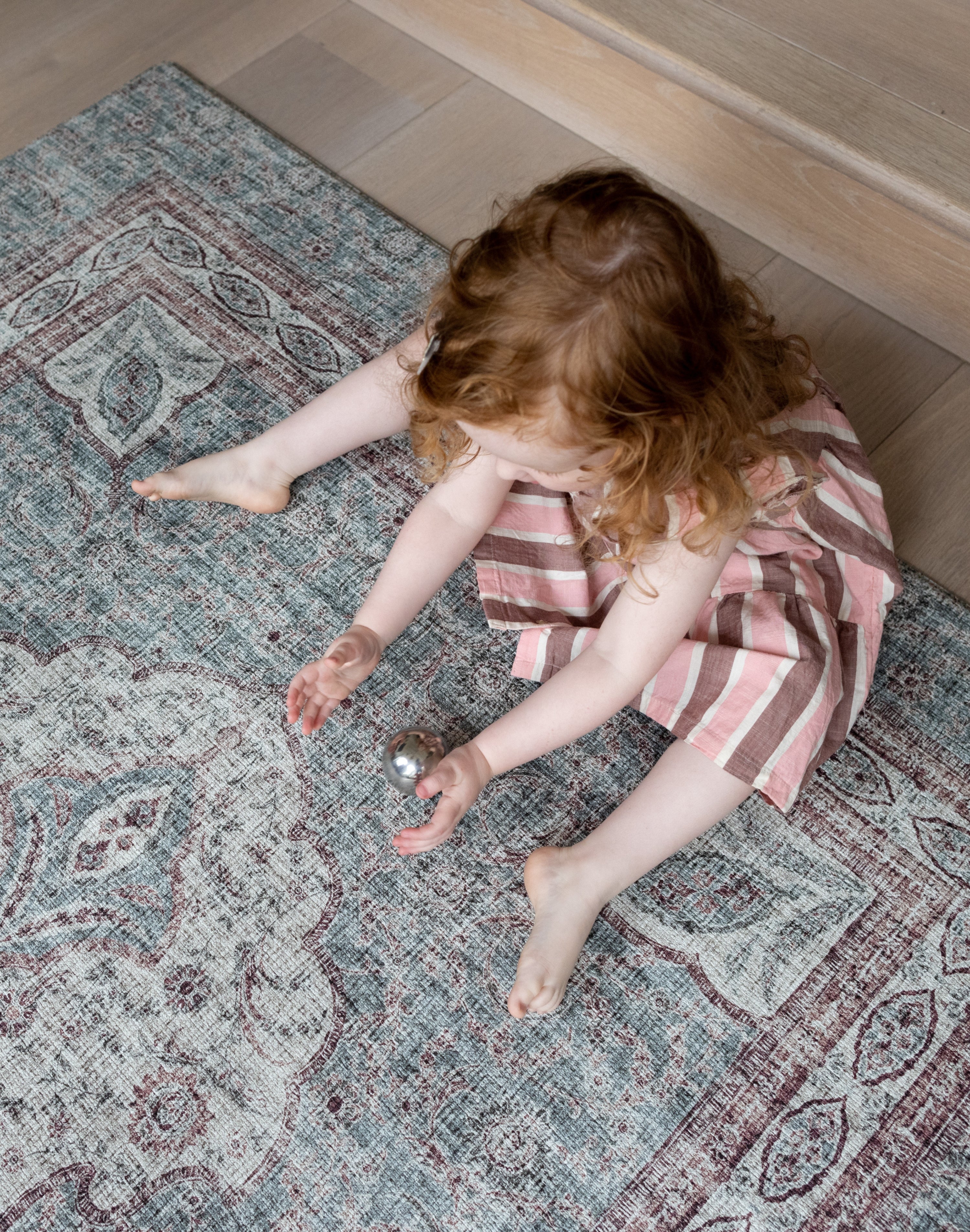 Toddler sitting on Totter + Tumble rug like playmat in a stylish lounge setting.