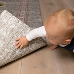Baby lifting edge of Totter + Tumble play mat showing non-slip backing and a new design on the reverse