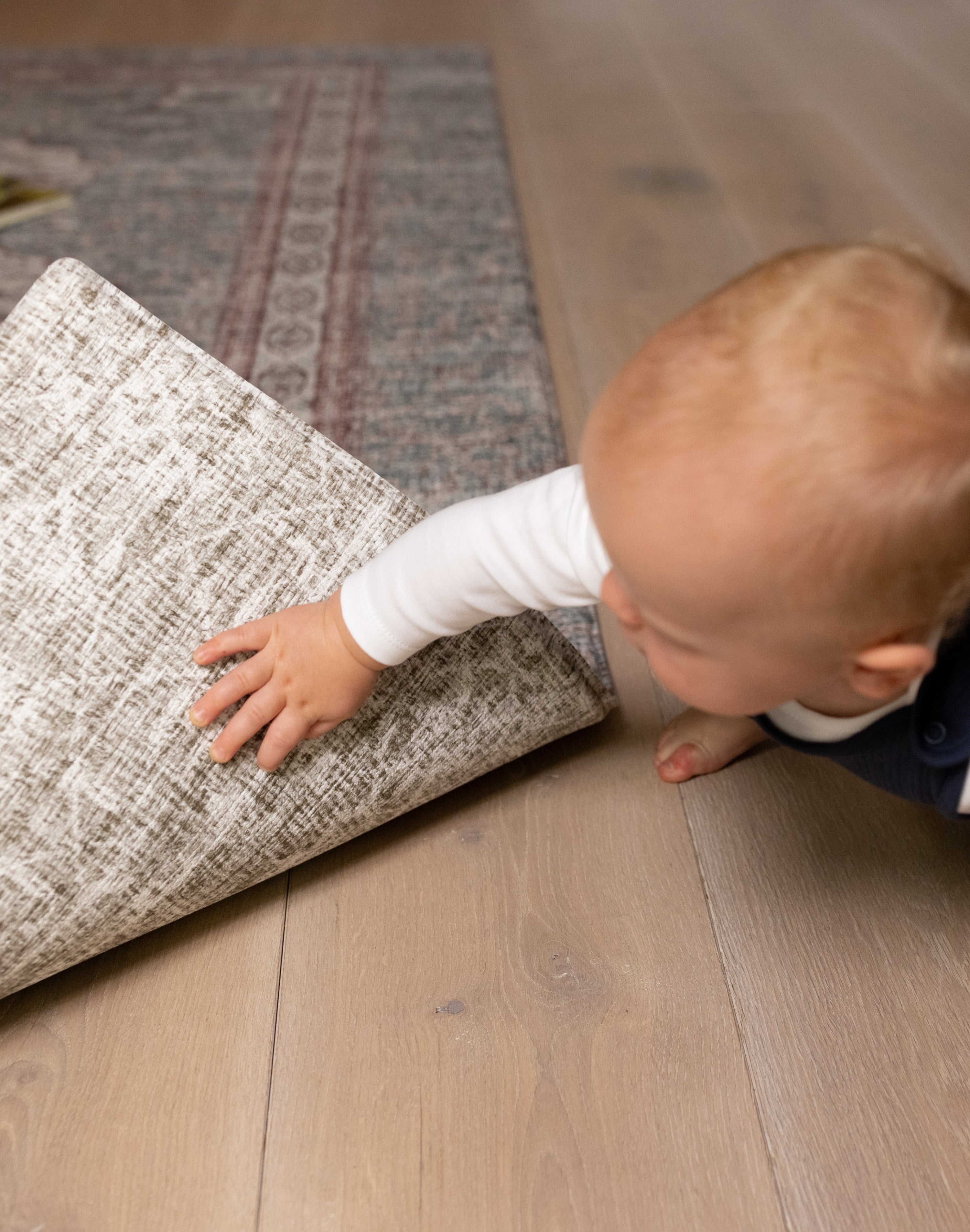Baby lifting edge of Totter + Tumble play mat showing non-slip backing and a new design on the reverse