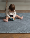 Baby sits up on Eclipse play mat for hard wood flooring and enjoys exploring wooden beaded baby toy
