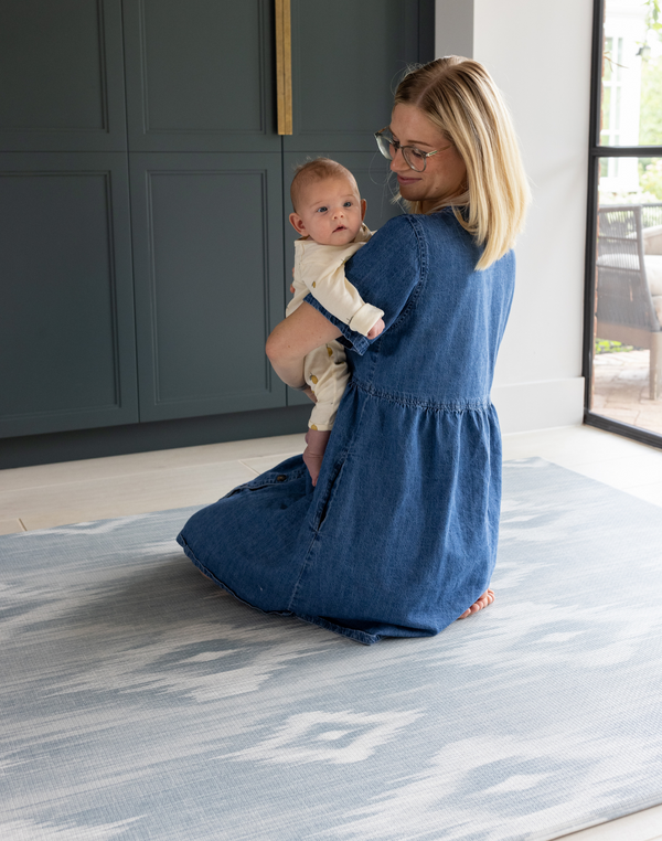 Mom and baby sitting on Thick padded play mats by totter and tumble are perfect for the smallest members of the family The Atlas has a hand drawn Ikat design in modern light blue and beige shades 