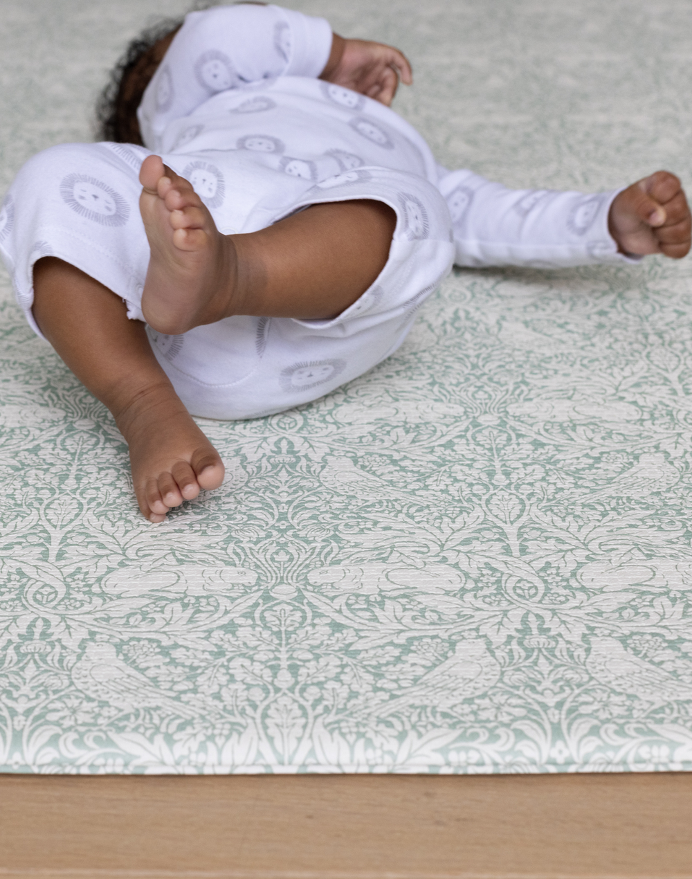totter + tumble brer rabbit play mat in morris & co design with baby laying on top, playing, rolling on supportive safe non toxic floor mat in padded memory foam to support and protect