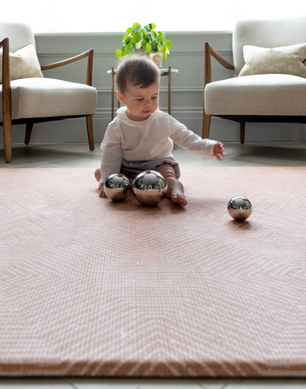 Baby sits on padded play mat enjoying playtime with metallic sensory toys