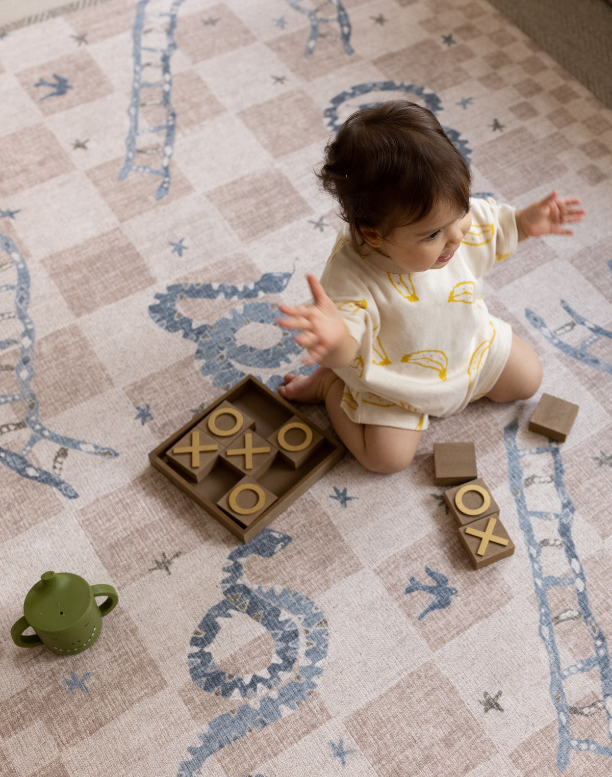 Baby sitting and playing on a neutral-toned luxury one-piece play mat with soft illustrated details in a light-filled home