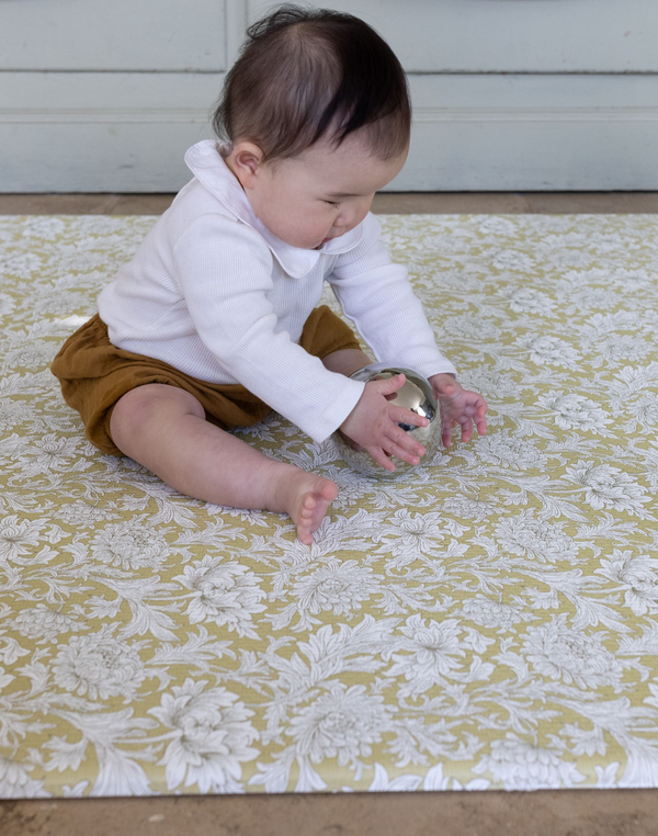 Baby playing with a metallic ball on the Chrysanthemum design heritage motif playmat by Totter and Tumble