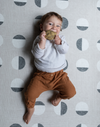 Little baby relaxes on a thick padded play mat while chewing on non toxic teething toy