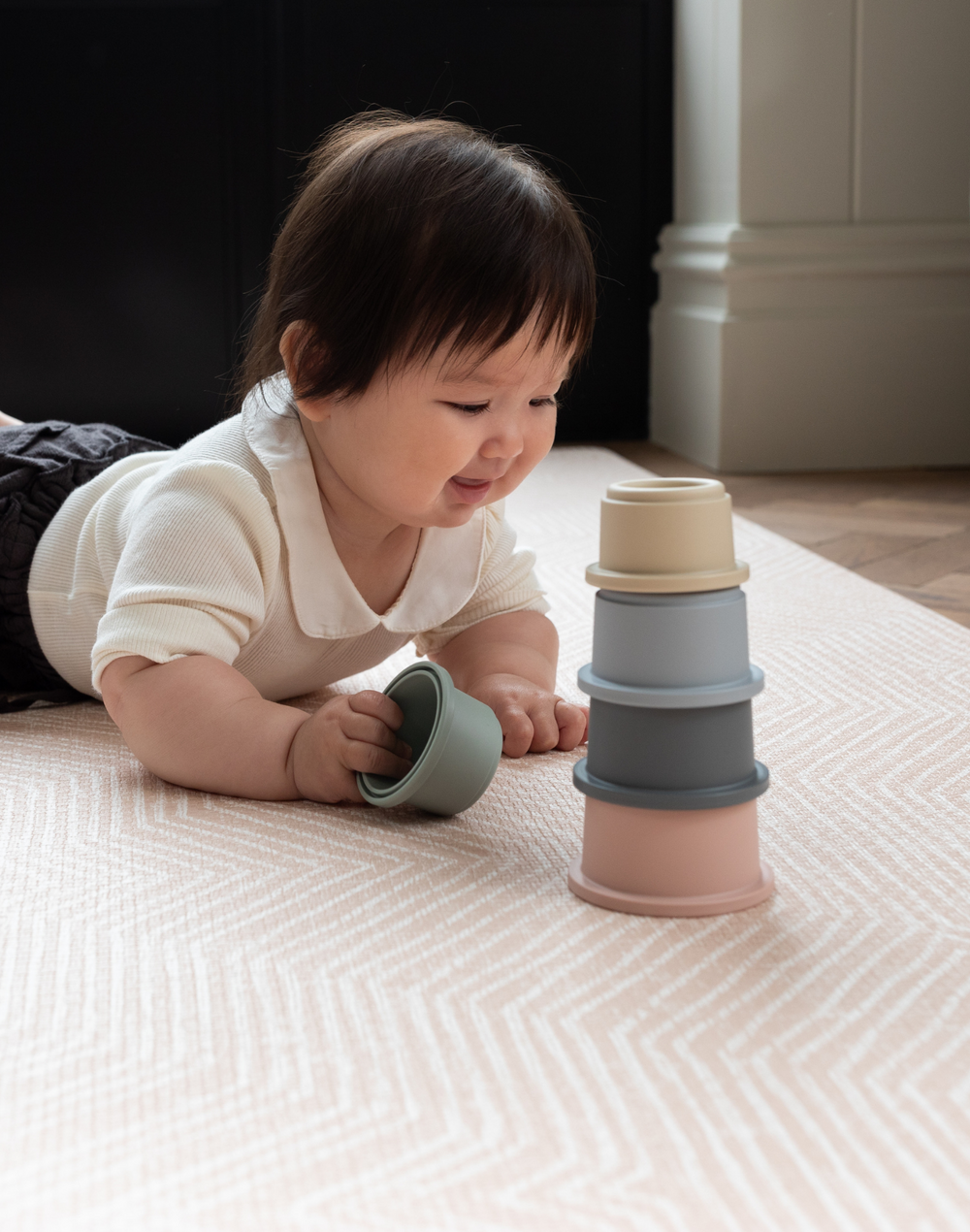 Baby stacks cups on soft toddler play mat designed to be safe from birth