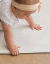 Baby girl crawls across the protective Globe Trotter baby play mat that supports babies development