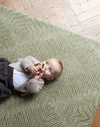 Baby enjoys floor time on the cushy play rug with a stylish olive textile design