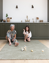 Little girl and grandmother enjoy playing with wooden skittles on a thick kitchen mat large in size for play time