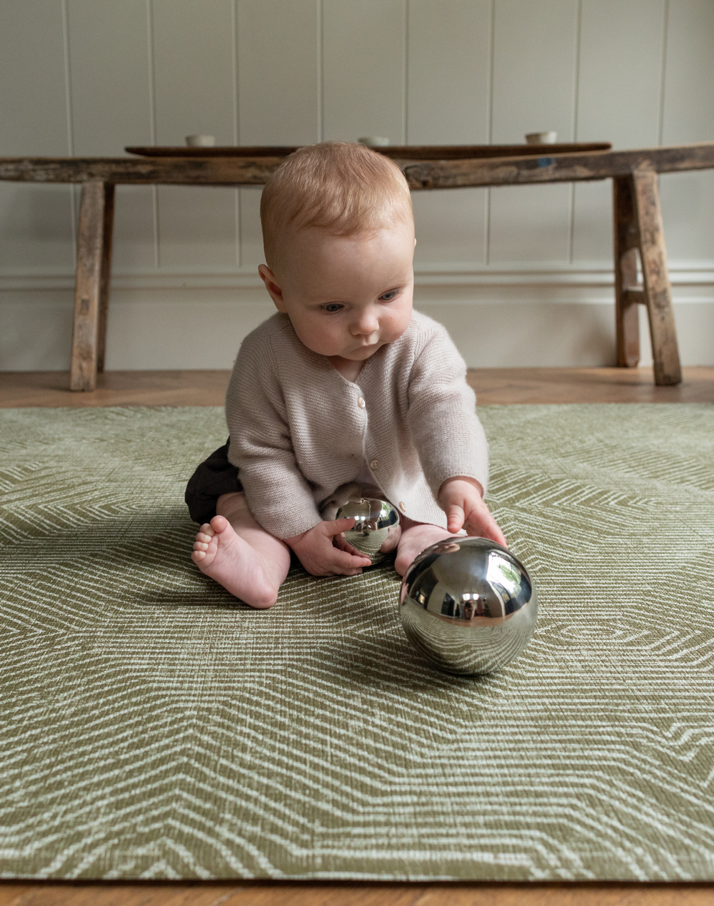 Baby enjoys playing with shiny sensory toys and is supported by the green floor rug by Totter and Tumble