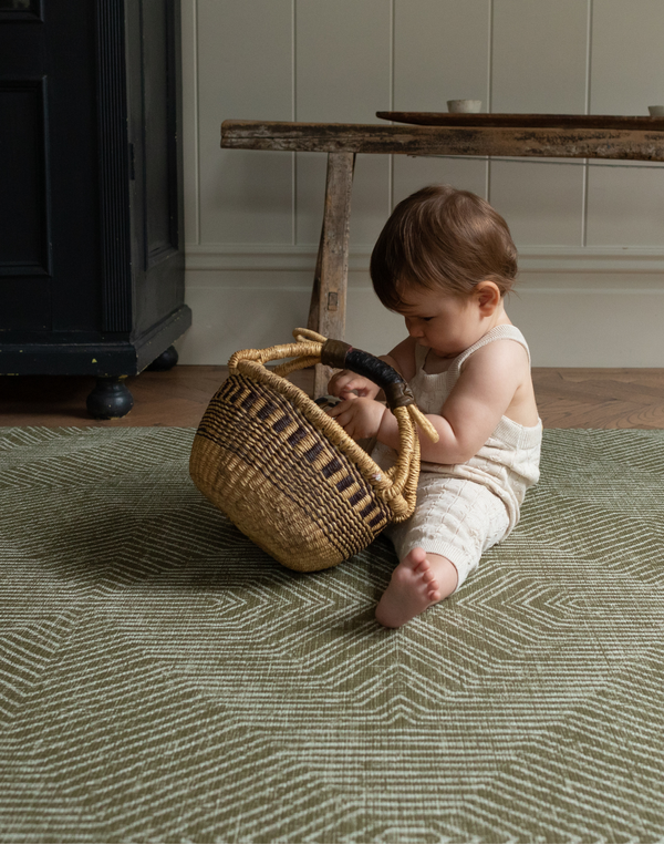 Baby enjoy play time with a basket on the cushy baby play mat with a contemporary green kilim design