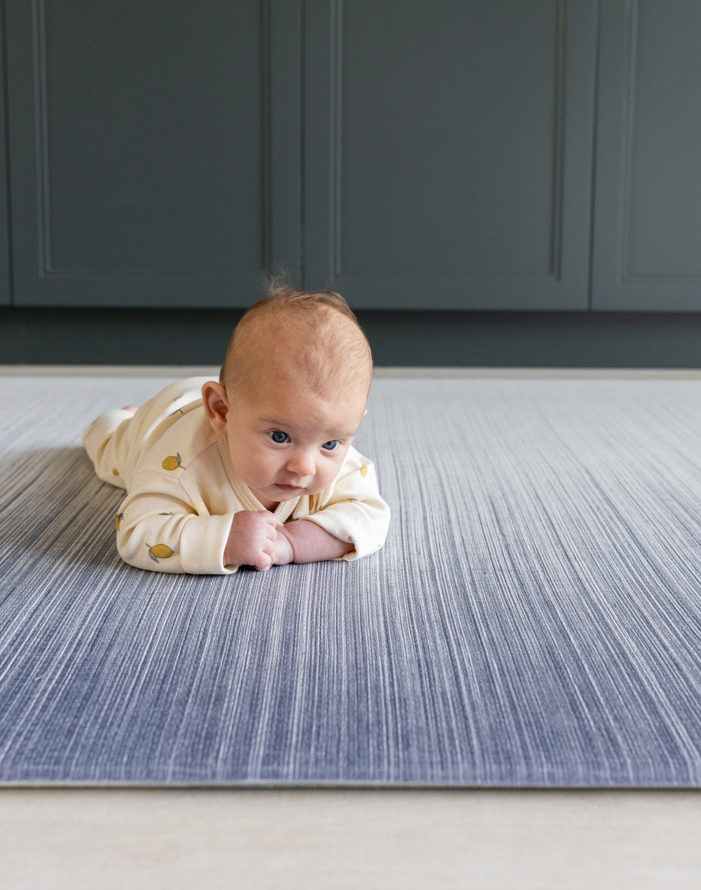 Baby enjoying tummy time on The Kasuri a large padded floor mat by Totter and Tumble adds a stylish appeal to the space it is unrolled in with a one piece design that is washable so spillages are easy to clean the perfect play rug for the home