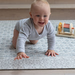 Smiling baby crawling on stylish gray play mat with colorful blocks