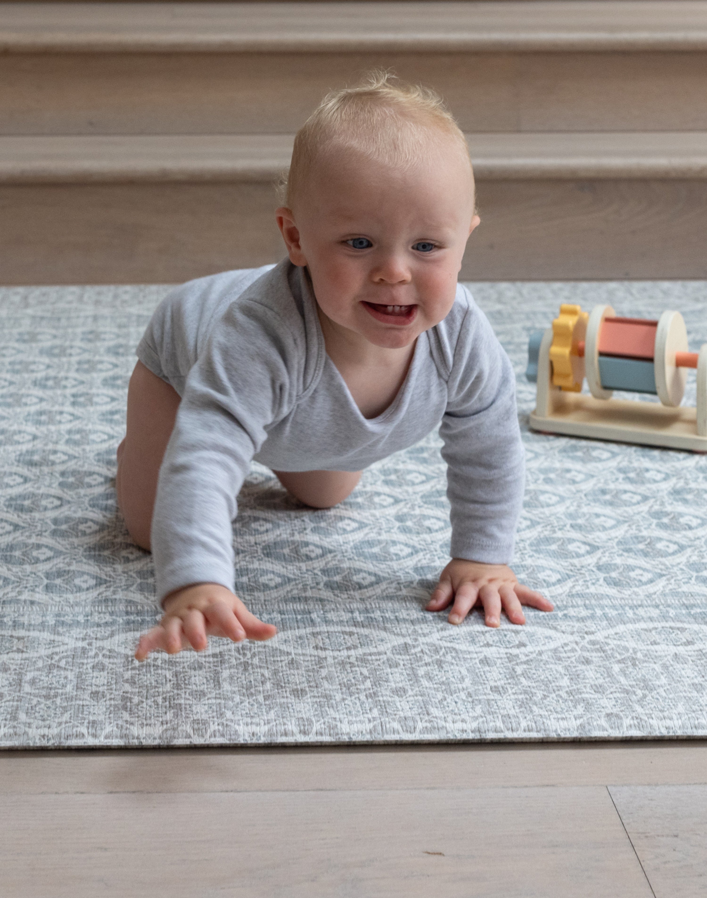 Smiling baby crawling on stylish gray play mat with colorful blocks