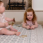 Two toddlers sitting on soft blue baby rug by a fireplace