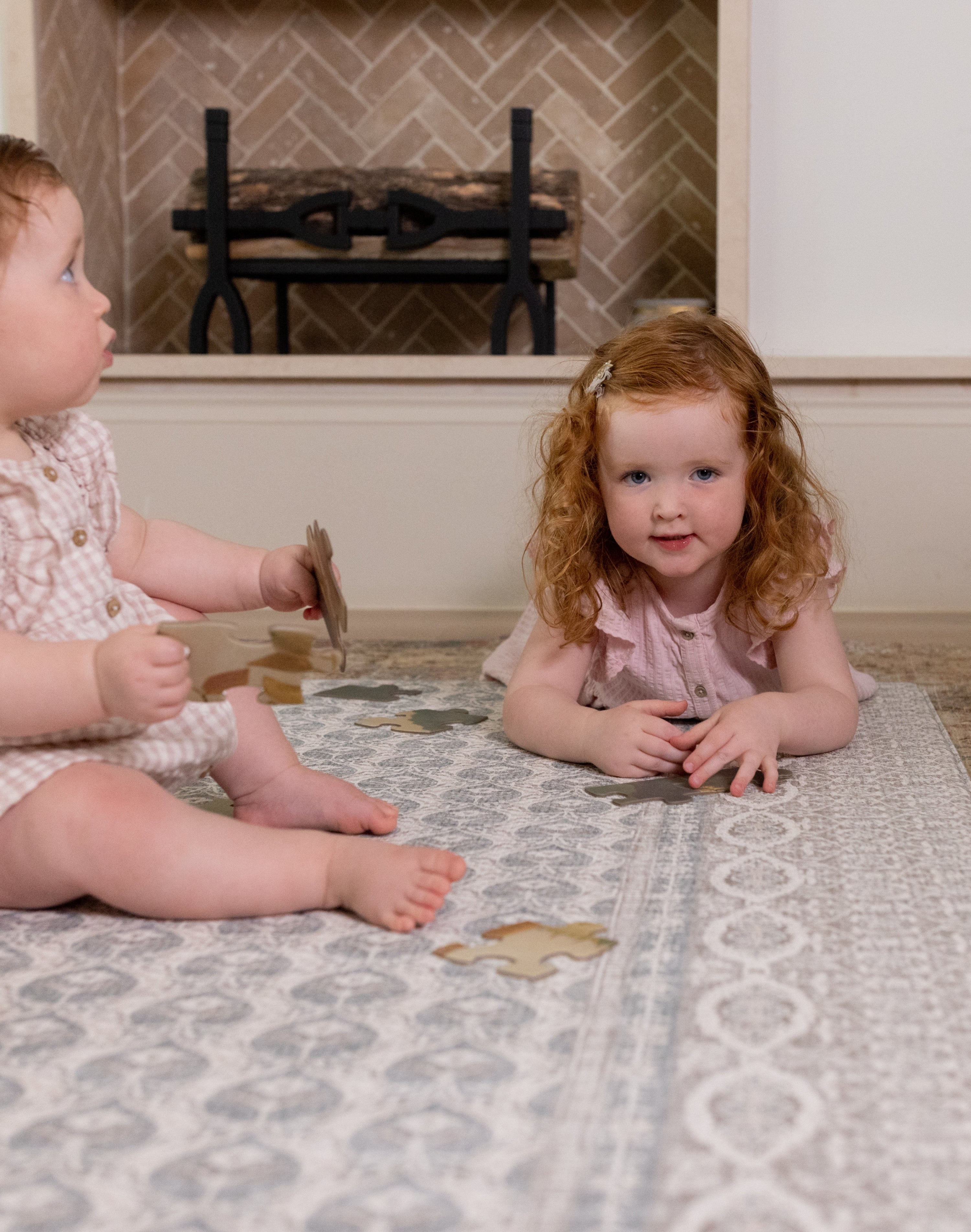 Two toddlers sitting on soft blue baby rug by a fireplace