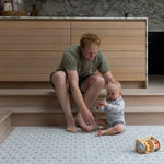 Parent and baby sitting together on large grey and blue play mat