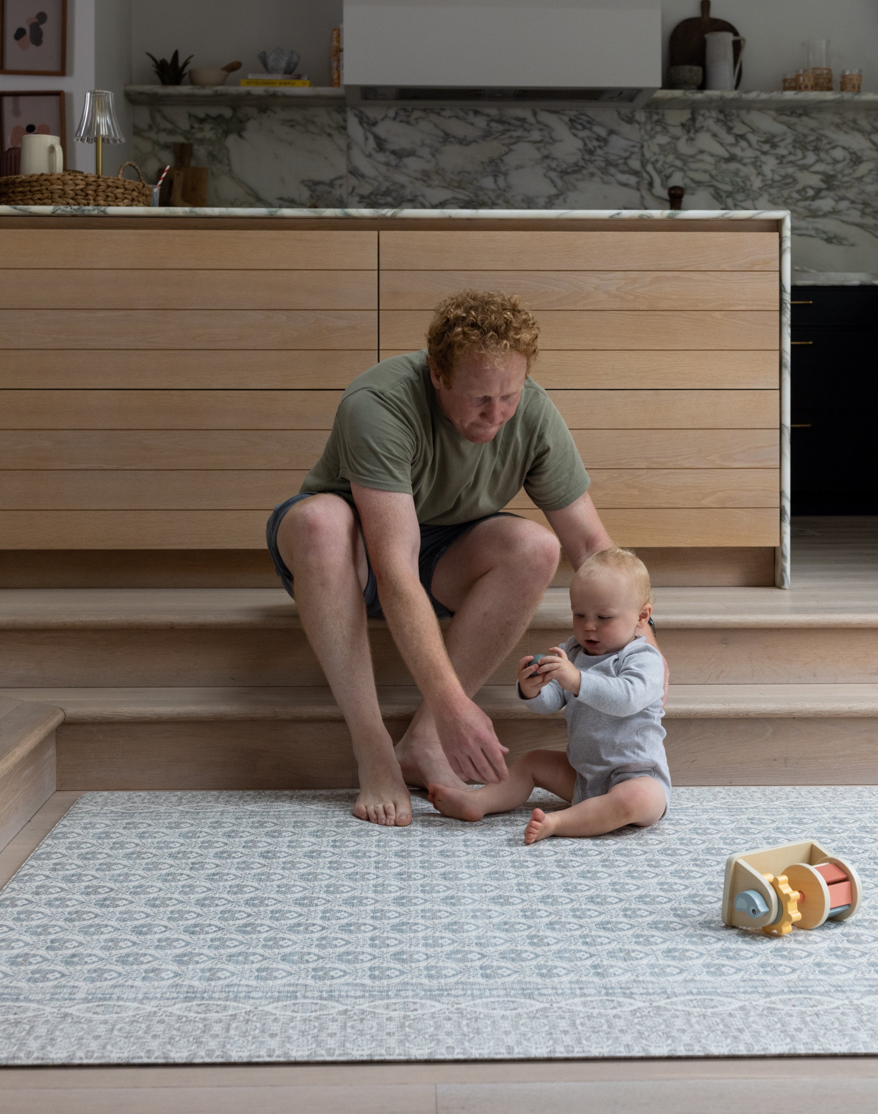 Parent and baby sitting together on large grey and blue play mat