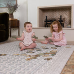 Two young children playing on an elegant Totter + Tumble play mat in a living room