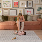 A mom sitting on a couch with a child on the floor in a living room with a large play mat