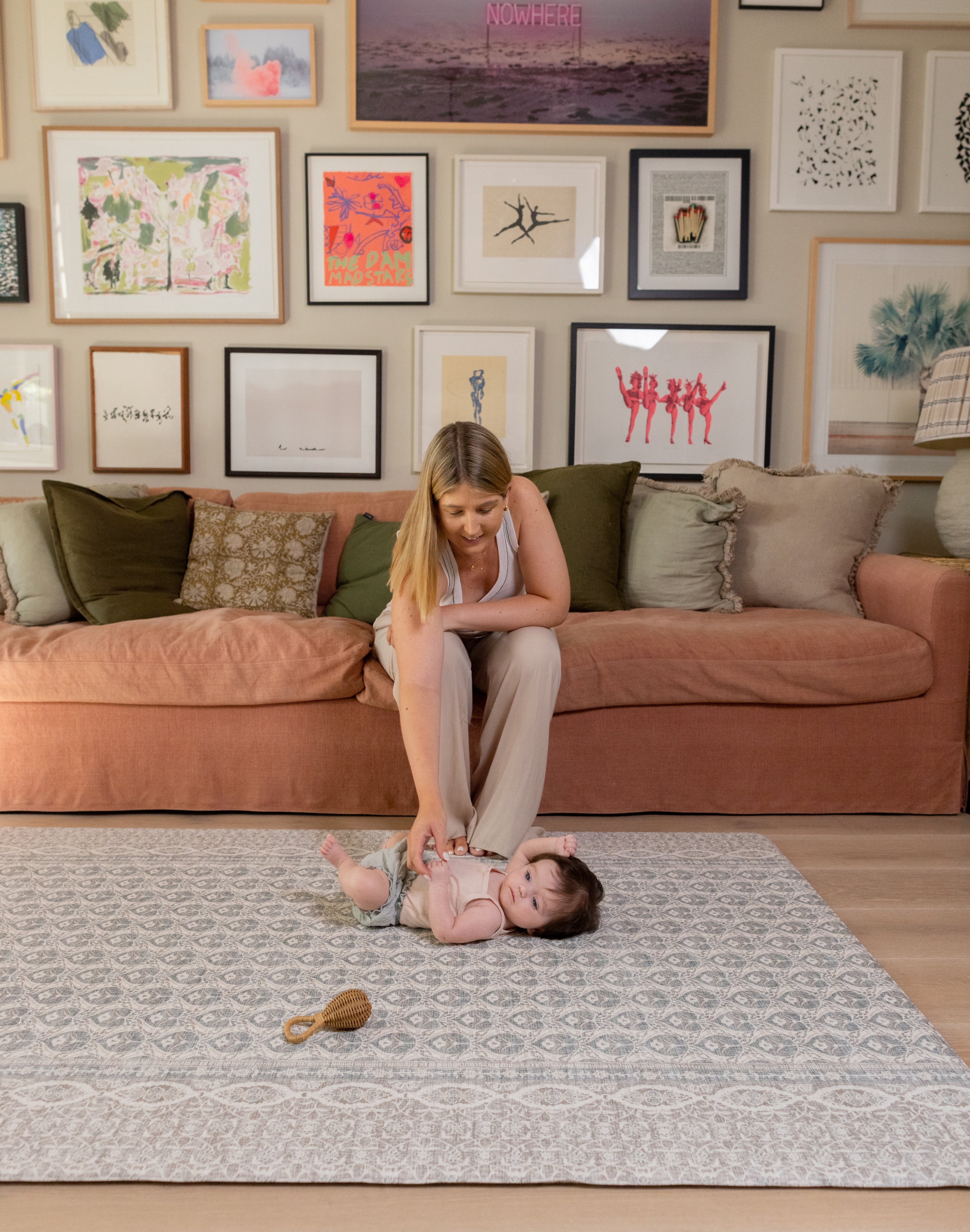 A mom sitting on a couch with a child on the floor in a living room with a large play mat