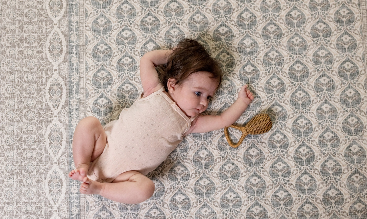 Baby lying on a patterned rug play mat with a rattle toy