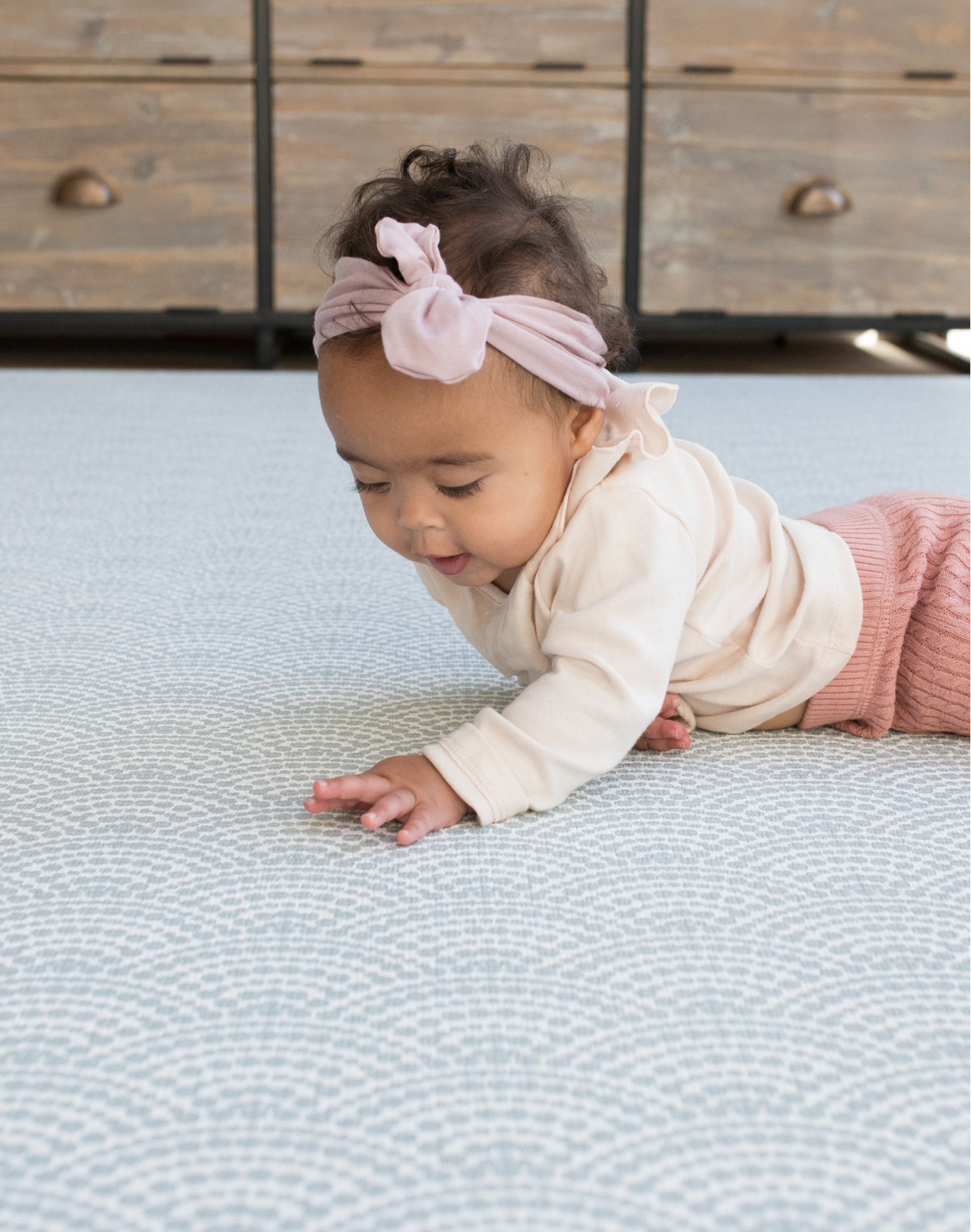 Little girl lays on stomach supported by memory foam playmat with a modern scalloped pattern in fresh blue colours