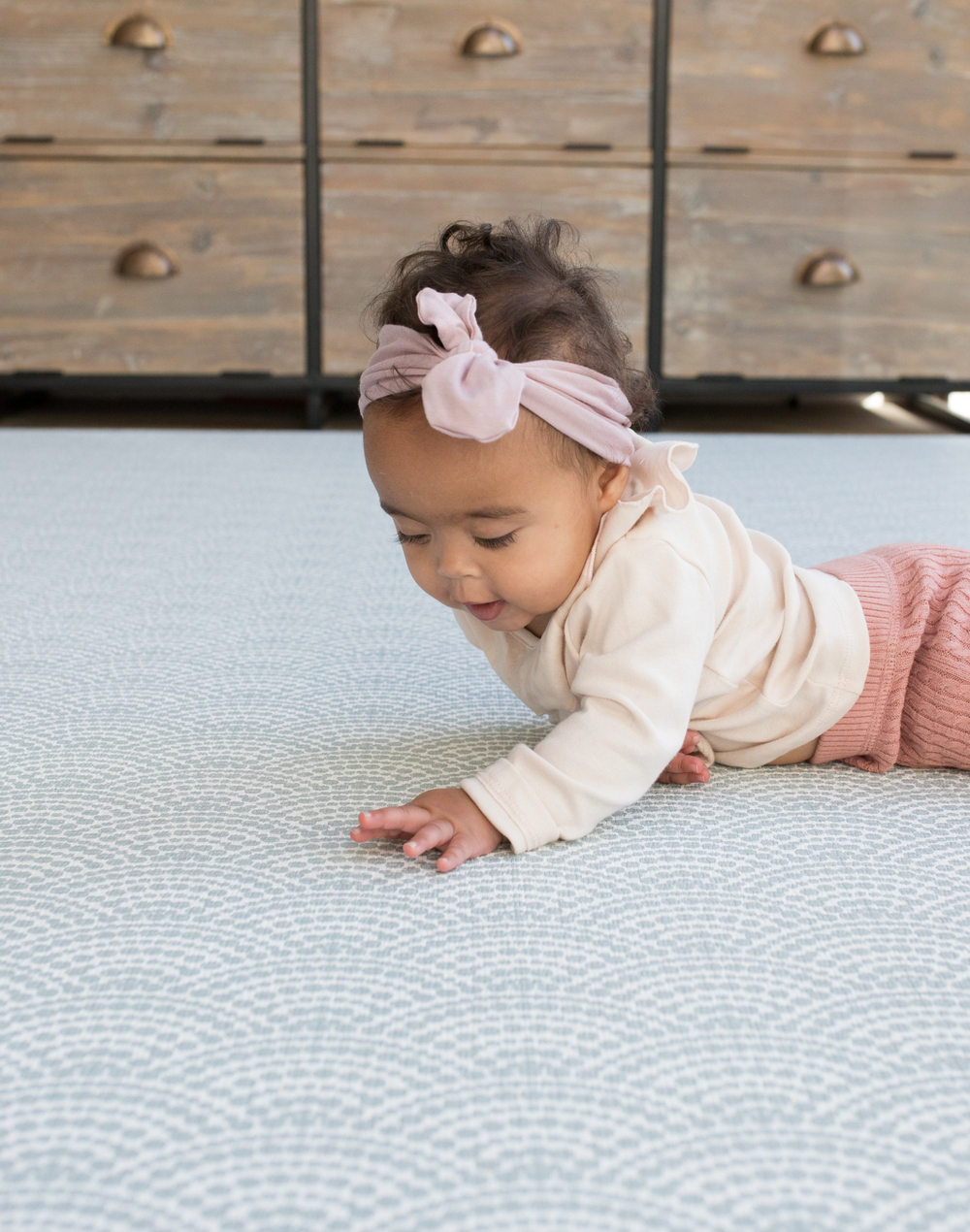Little girl lays on stomach supported by memory foam playmat with a modern scalloped pattern in fresh blue colours