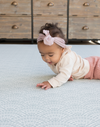 Little girl lays on stomach supported by memory foam playmat with a modern scalloped pattern in fresh blue colours